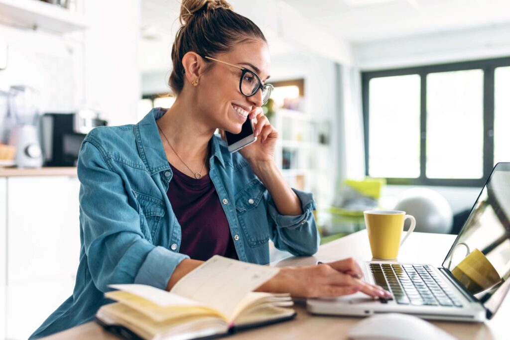 Self-employed woman working on a laptop while talking on the phone at home